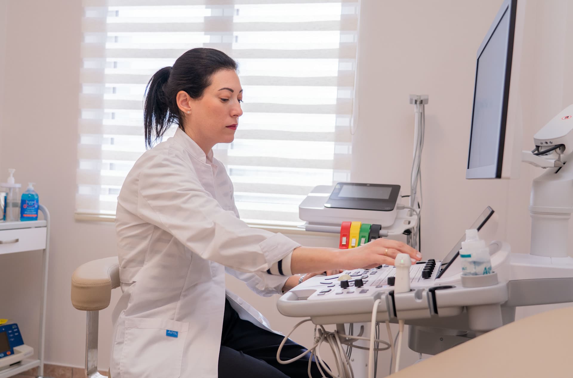 Ιατρός στο εξεταστήριο, καθισμένη σε καρέκλα, κοιτάζει το πληκτρολόγιο του εξοπλισμού εξέτασης.