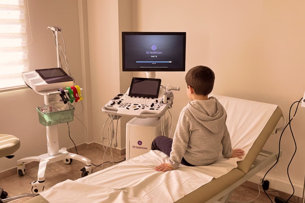 Ενα παιδί κάθεται στο κρεβάτι εξέτασης περιμένοντας τη γιατρό