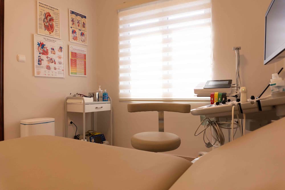 Το δωμάτιο εξέτασης όπως φαίνεται από το κρεβάτι εξέτασης, με τον εξοπλισμό και εικόνες ανατομίας της καρδιάς στον τοίχο